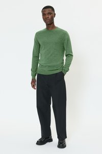 Roheline soonikuga ümara kaelusega kampsun, kombineeritud mustade laiade pükstega ja mustade pits-up saapadega. Siledat tekstuuri, õlgade juures vormitud.