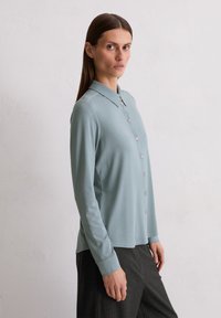 Jasnoniebieska, zapinana na guziki koszula z kołnierzykiem, z długimi rękawami i gładką teksturą. W połączeniu z ciemnymi spodniami w prążki.