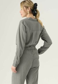Čierno-biely vzorovaný outfit pozostávajúci z voľného topu s dlhými rukávmi a nohavíc s elastickým pásom. Hladká textúra s geometrickým dizajnom.