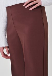 Bruine high-waisted broek van een gladde, stevige stof; de op maat gemaakte pasvorm en minimale details benadrukken de strakke lijnen en het moderne ontwerp.