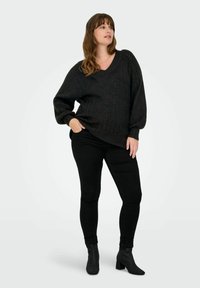 Čierny, oversized pletený sveter s výstrihom do V, s dlhými rukávmi a textúrovanou látkou, spárovaný s čiernymi úzkymi džínsami a členkovými topánkami.