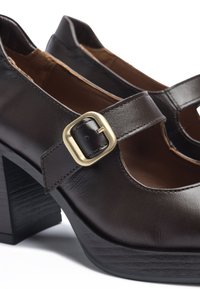 Zapatos de tacón alto de cuero marrón con un tacón de bloque negro. Presentan una sutil correa con hebilla en la parte delantera y un diseño recortado.