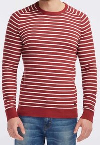Maglione a righe rosse e bianche con collo rotondo, polsini e orlo a coste. Realizzato in un materiale a maglia testurizzato. Indossato con jeans blu.