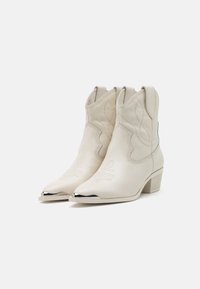 Botas de vaquero de cuero blanco con punteras puntiagudas, costuras decorativas y acentos en tono plateado en la puntera. Incluyen tacones de bloque de altura media.