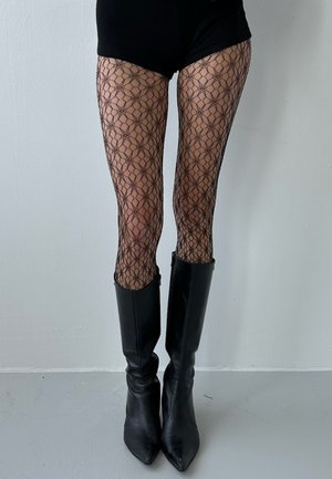 Collants noirs à motif géométrique, portés avec de grandes bottes en cuir noir à bout pointu et finition élégante.