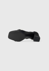 Scarpa nera con tomaia in tessuto testurizzato, tacco quadrato e suola in gomma liscia. Il design presenta uno stile minimalista senza decorazioni.