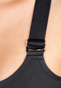 Zwarte sportbeha-band met verstelbare schuifsluiting, een gladde textuur en een gebogen randontwerp. Close-up afbeelding van het bevestigingspunt van de band.