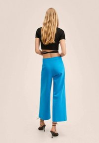 Pantalons larges bleus en tissu lisse, avec une taille haute et des détails à cordon. Associés à un crop top noir ajusté.