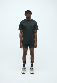 T-shirt et shorts de sport noirs, associés à des chaussettes noires Nike et des sneakers blancs. La casquette est gris clair avec un logo. Design et coupe simples.