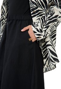 Lange zwarte rok met elastische tailleband, gecombineerd met een witte shirt met zwart zebra print ontwerp. Klein logo label op de zak.