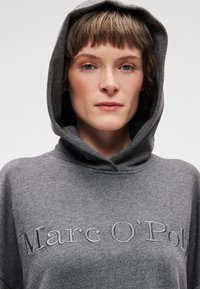 Šedá mikina s kapucí s vyšitým nápisem "Marc O'Polo", vyrobená z měkké látky. Nabízí volný střih a výrazný design kapuce.
