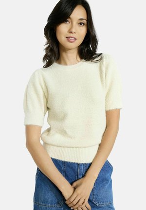 Un pullover en maille texturée couleur crème, à manches courtes bouffantes et ourlet côtelé, associé à un bas en denim.