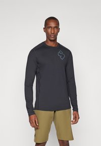 Zwarte, vochtregulerende shirt met lange mouwen en een ronde halslijn, voorzien van een subtiele logo, gecombineerd met olijfgroene shorts. Rekbare stof; gladde textuur.