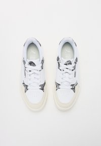 Baskets blanches avec accents en imprimé serpent noir, matériau léger, conception à lacets et semelle en caoutchouc beige. Texture lisse et bout perforé.