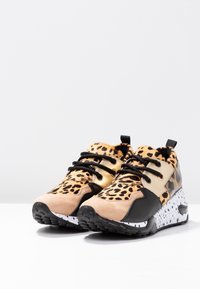 Baskets chunky avec imprimé léopard, embout noir, côté métallique doré, lacets noirs et semelle blanche avec des speckles noirs.