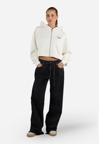 Felpa bianca con cappuccio, a maniche lunghe e chiusura con zip, con dettagli ricamati, abbinata a jeans neri a vita alta con gamba larga e scarpe beige slip-on.