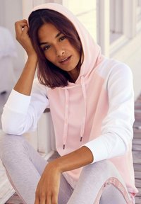 Hoodie rosa chiaro e bianco con tasca frontale e cordini, abbinato a leggings grigio chiaro con una striscia logo rosa. Tessuto dalla texture liscia.