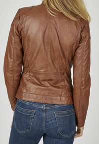 Giacca di pelle marrone con un design aderente, cuciture visibili e tasche laterali. Indossata con jeans in denim blu dotati di tasche posteriori.