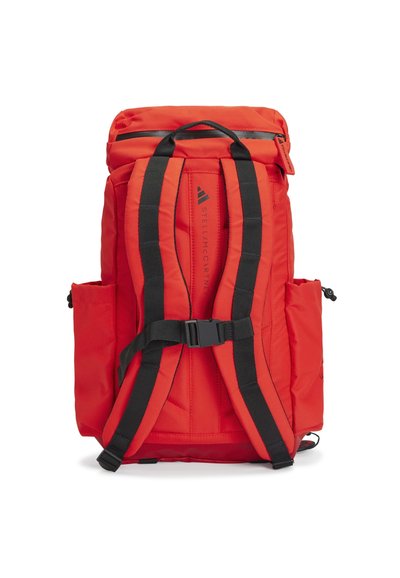 Red backpack with quilted texture, black adjustable straps, top flap, side pockets, and front buckle closure. Features branding on back.