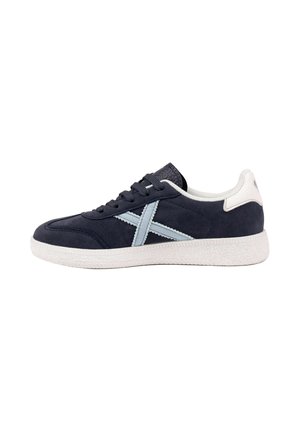 Zapatilla negra y blanca con detalle de cruz azul claro en el lateral y suela blanca texturizada, vista desde el lado exterior.