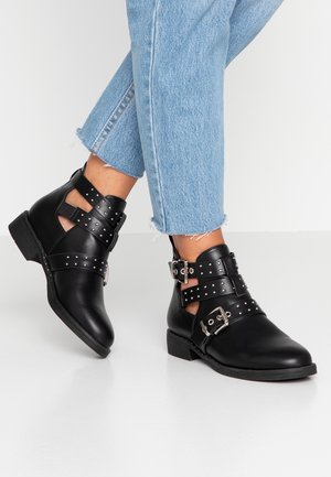 Bottes noires en cuir, ornées de clous argentés, avec plusieurs sangles et boucles. La semelle est basse avec un petit talon ; conçue avec des découpes.