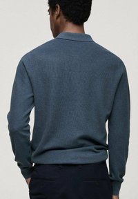 Tmavě modrá polokošile s dlouhým rukávem vyrobená z texturovaného pleteného materiálu, s klasickým límečkem a přiléhavým střihem.