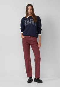 Tume svüẗer, millel on kirjas "NAUDI", valge kaelus, maroonid sirged püksid ja mustad robustsed kingad. Lihtne disain, igapäevaeluks sobivad materjalid.