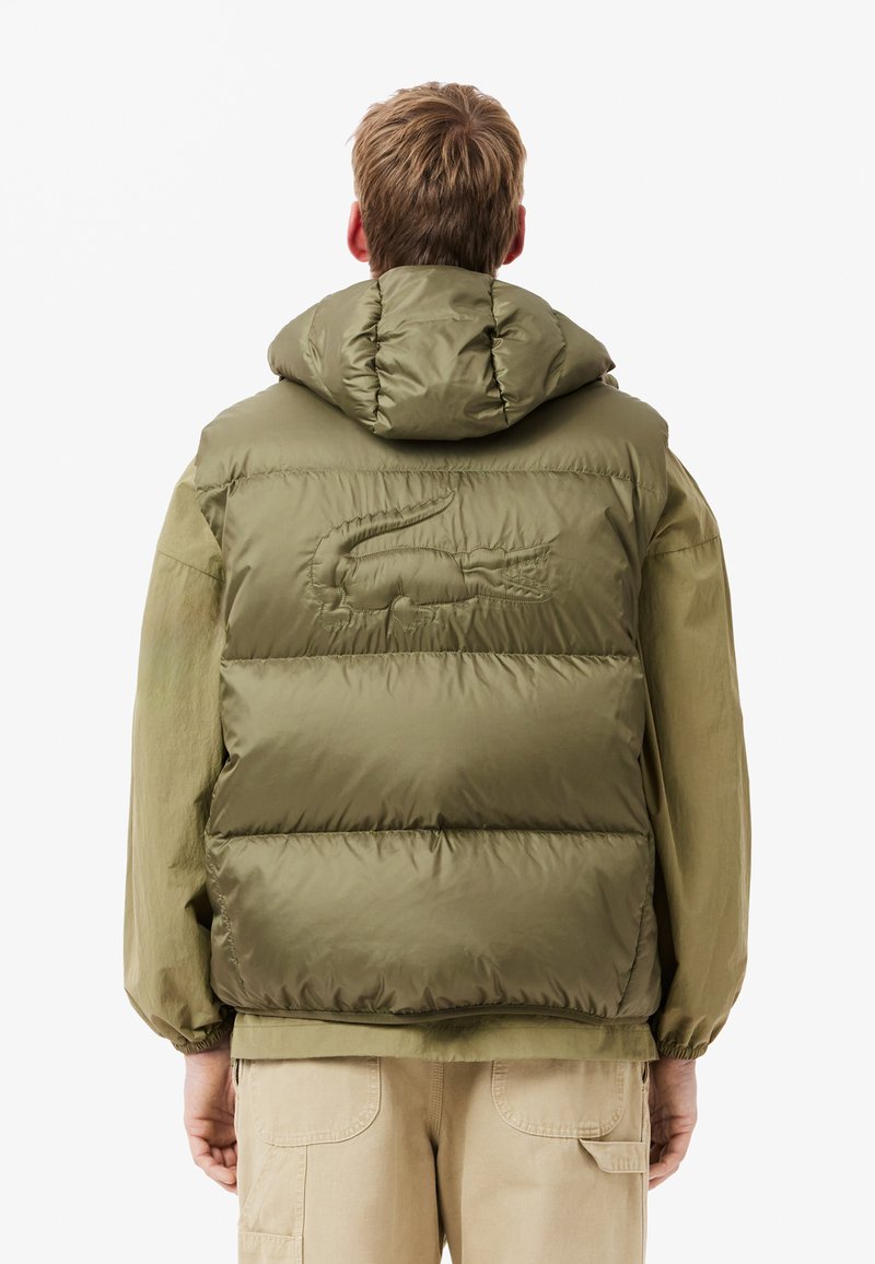 Chaqueta acolchada en verde oliva con diseño acolchado y capucha sobredimensionada. Presenta un logo en relieve en la parte trasera y puños elásticos.