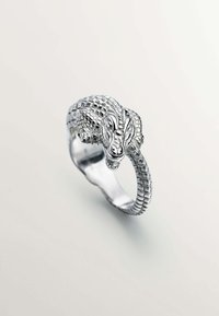 Anillo de plata con forma de caimán, que presenta escamas detalladas y una banda texturizada. La cabeza está posicionada de manera prominente en la parte superior.