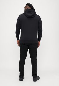 Czarna bluza z kapturem, wykonana z miękkiego materiału, zestawiona z dopasowanymi czarnymi dżinsami i czarnym obuwiem, prezentująca prosty design.