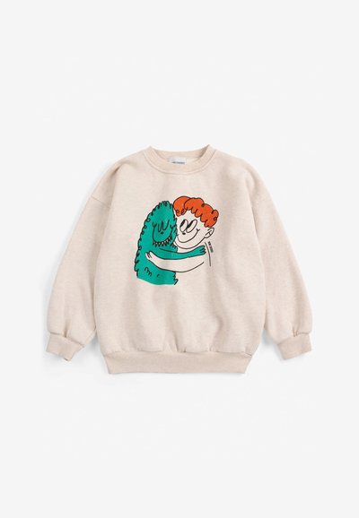 Sweat-shirt beige avec illustration d'une personne rousse étreignant un monstre vert souriant sur le devant.