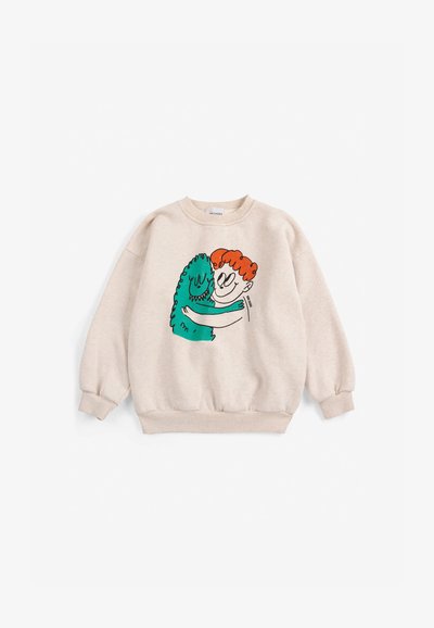 Sweat-shirt beige avec illustration d'une personne rousse étreignant un monstre vert souriant sur le devant.
