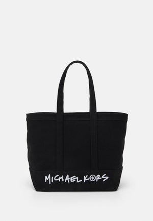 Sort tote taske med to håndtag og hvid "Michael Kors" logo tekst på den nederste forreste kant, sat mod en ensartet lys baggrund.
