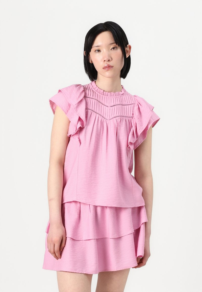 Haut rose superposé avec des manches volantes, des détails smockés et un col rond. Fabriqué en tissu texturé, conçu pour un ajustement ample.
