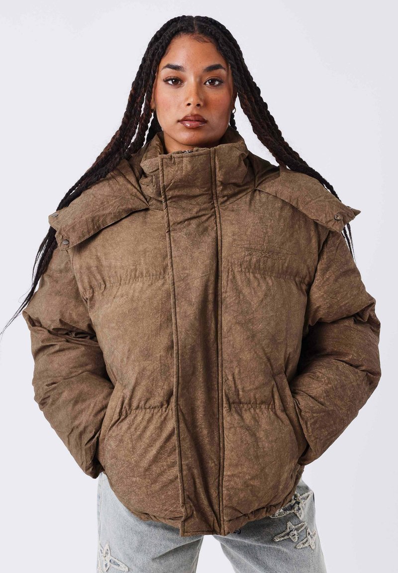 Chaqueta acolchada marrón con un cuello alto, que presenta una tela texturizada y grandes costuras prominentes. El diseño incluye botones a presión en los hombros.