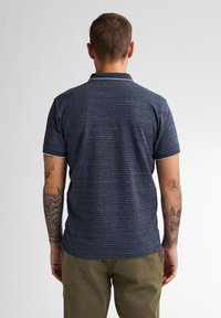 Polo de color navy con un patrón de rayas texturadas, de manga corta y con un ribete de color blanco en el cuello, hecho de una suave tela de punto.