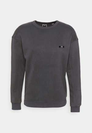 Sudadera gris oscuro con escote redondo, puños acanalados y una pequeña etiqueta de logo negra en el pecho. Tejido suave con una textura lisa.
