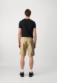 Camiseta negra de manga corta con logo, combinada con pantalones cortos beige de puño. El modelo lleva zapatillas negras y calcetines blancos. Un atuendo simple y casual.