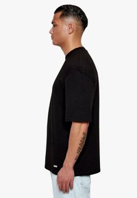 Black short-sleeve t-shirt made of cotton, featuring a crew neckline, loose fit, and a small logo tag at the bottom hem.
