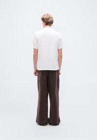 Λευκό βαμβακερό t-shirt με κοντά μανίκια, σε συνδυασμό με χαλαρά καφέ παντελόνια λινά με πίσω τσέπες και ίσια γραμμή.