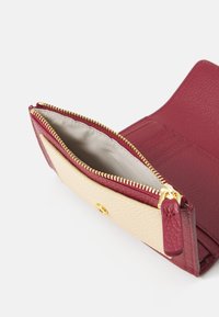 Bifold wallet with burgundy textured leather and cream smooth leather. Features a gold zipper and interior card slots. Open view shows inner lining.