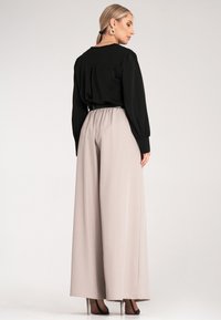 Czarna bluzka o luźnym kroju i długich rękawach, w połączeniu z jasnobeżowymi, szerokimi spodniami. Spodnie mają elastyczny pasek w talii i gładką teksturę.