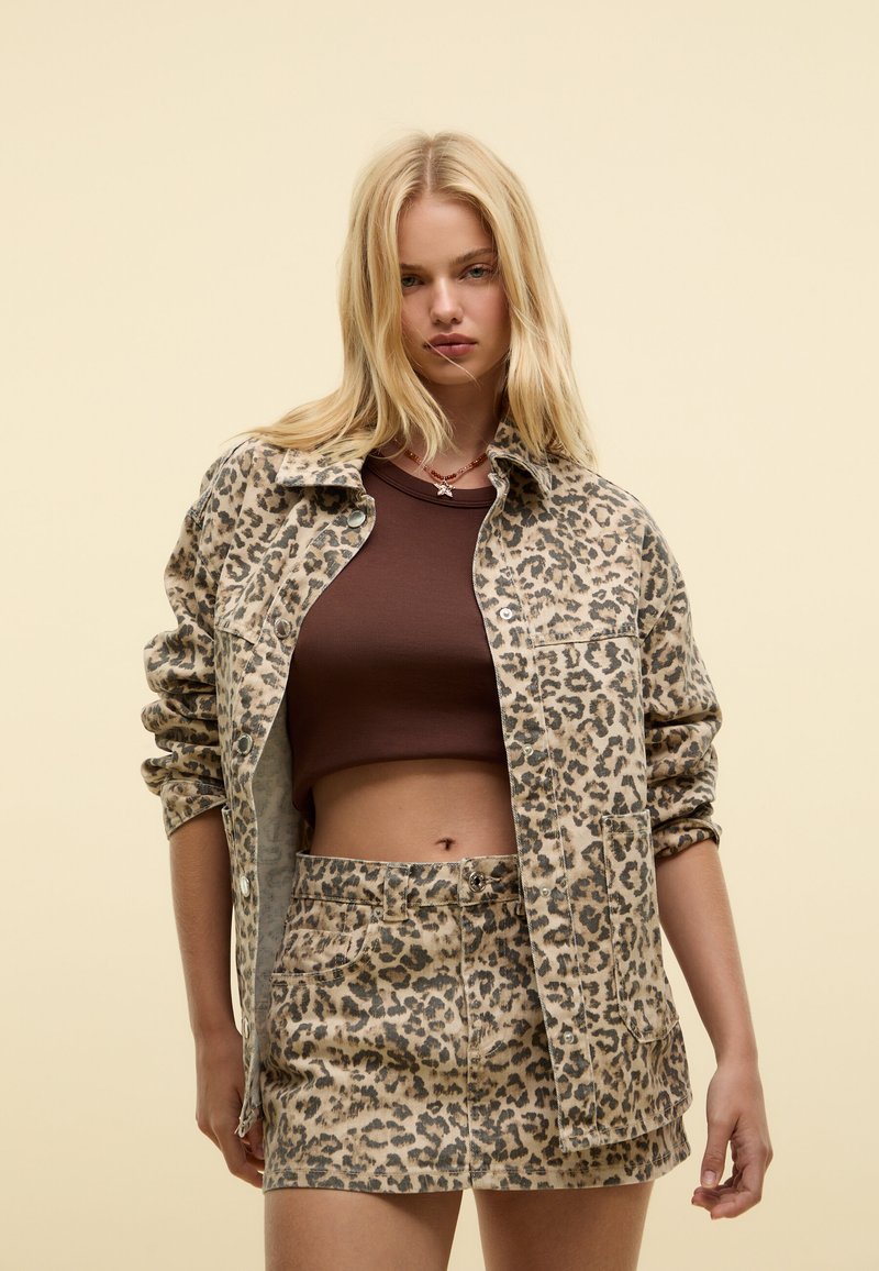 Veste courte à imprimé léopard avec une coupe décontractée, associée à une mini-jupe assortie à imprimé léopard. Débardeur marron en dessous.
