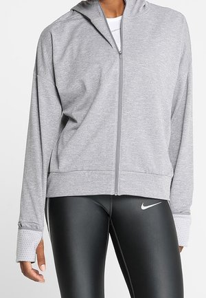 Grauer Reißverschluss-Hoodie mit lockerer Passform, ausgestattet mit einer Kapuze und gerippten Bündchen, kombiniert mit schwarzen Leggings, die ein weißes Logo tragen.