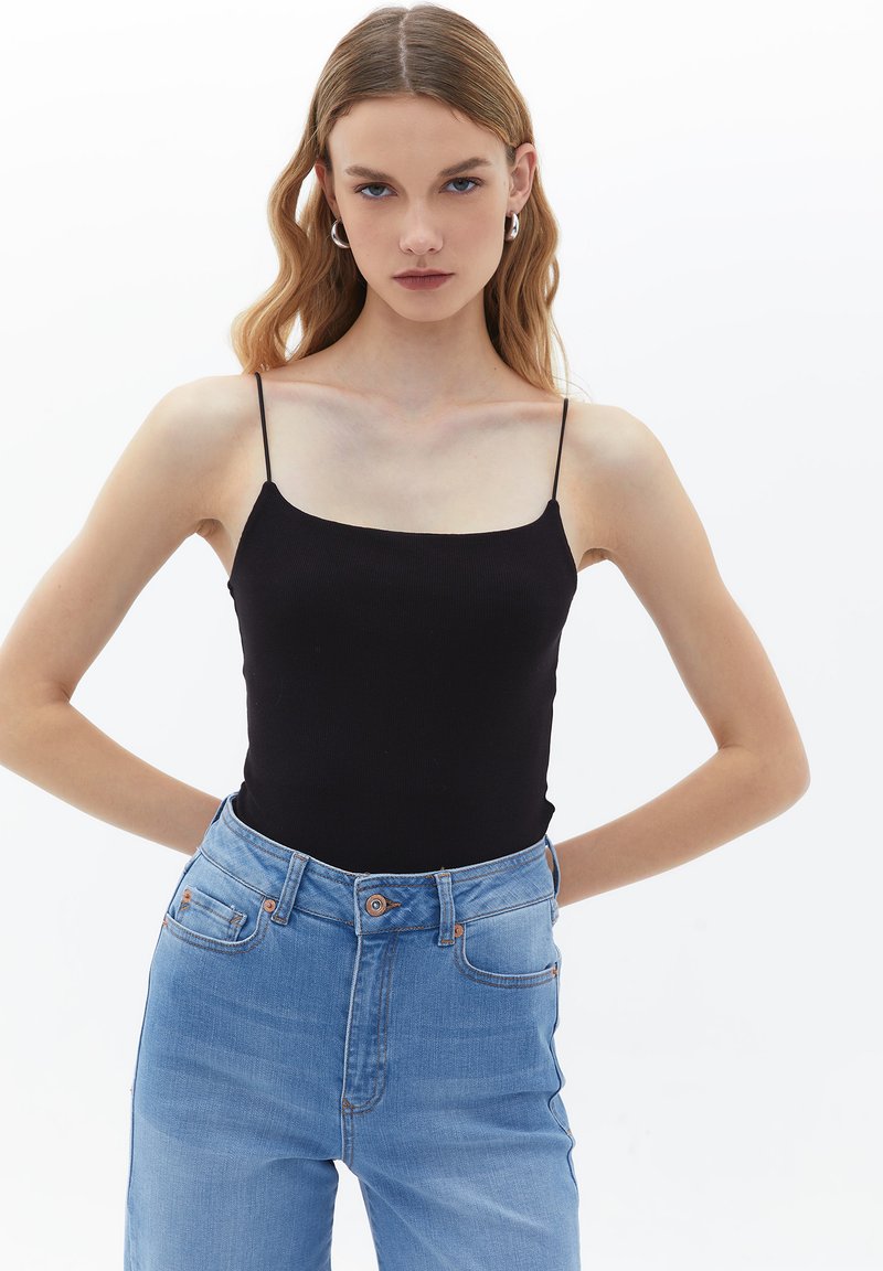 Top a maniche corte nero a costine con spalline sottili, abbinato a jeans azzurri a vita alta. Texture liscia e design aderente con dettagli minimi.