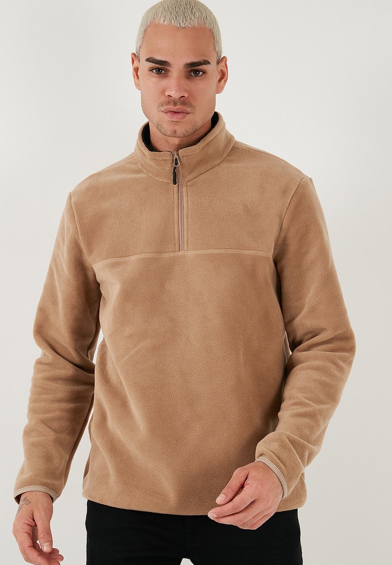 Pullover in pile color sabbia con collo mezza zip e maniche lunghe. Presenta una texture liscia e un colore uniforme senza motivi o accenti.