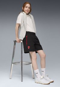 Pantaloni sportivi neri con dettagli rossi, una felpa grigia senza maniche e una T-shirt bianca. Indossati con scarpe da ginnastica bianche e calze fino al ginocchio.