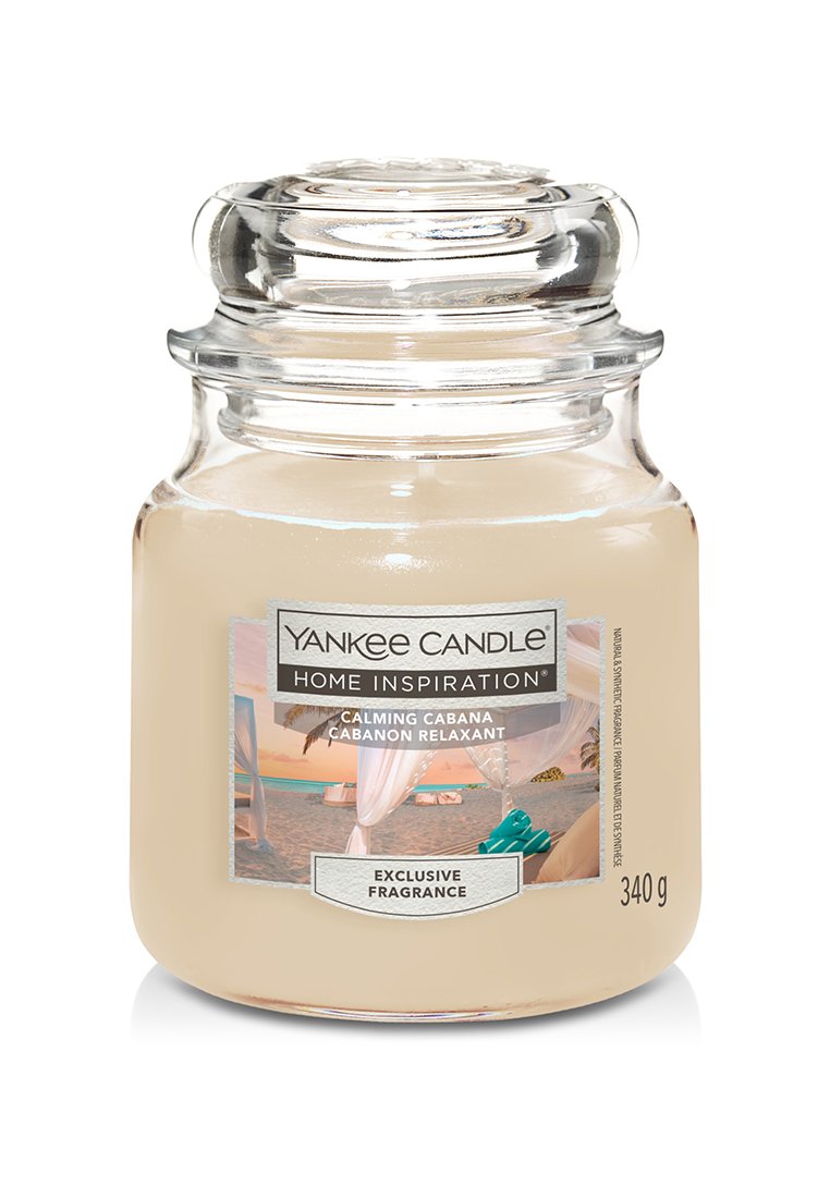 Bougie en bocal en verre transparent avec un couvercle rond, remplie de cire beige. L'étiquette présente une image et le texte "Yankee Candle Home Inspiration : Calming Cabana."