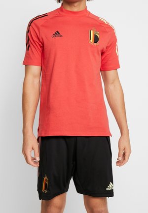 Camiseta deportiva de manga corta roja con cuello alto, con rayas negras y un emblema del equipo nacional de Bélgica. Combinada con pantalones cortos negros y detalles en dorado.