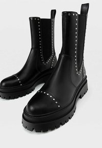 Bottines en cuir noir avec détails cloutés, bout arrondi et semelle crantée épaisse. Elles sont équipées de panneaux latéraux élastiques et d'une languette pour un enfilage facile.
